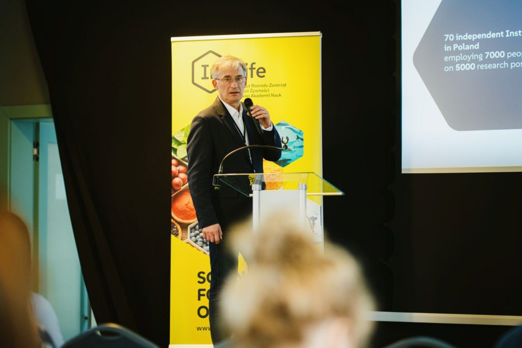 Prelegent przemawiający z mikrofonem przy ambonce na tle ścianki InLife PAN podczas Living Labs.