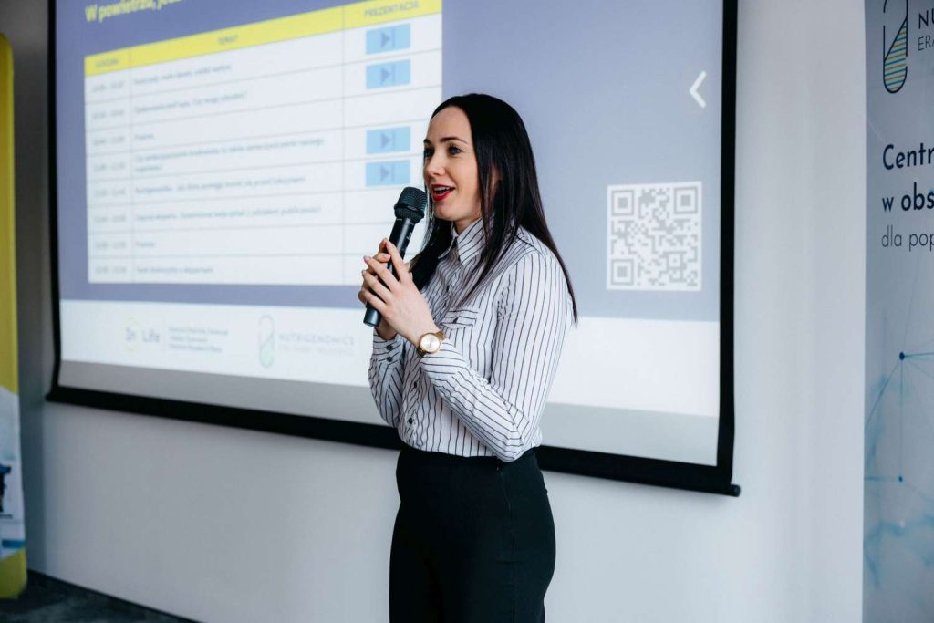 Prelegentka z mikrofonem przemawiająca przed ekranem z prezentacją na seminarium InLife.