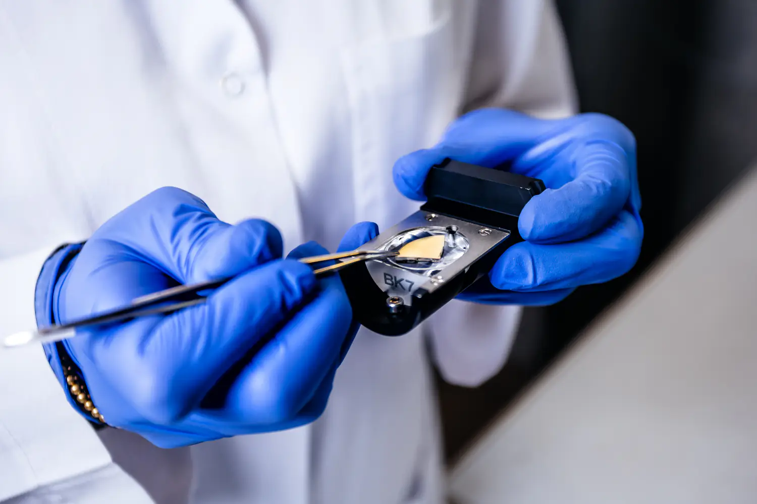 Badacz nakładający pęsetą miniaturowy biosensor do uchwytu pomiarowego w laboratorium bioelektroanalityki.