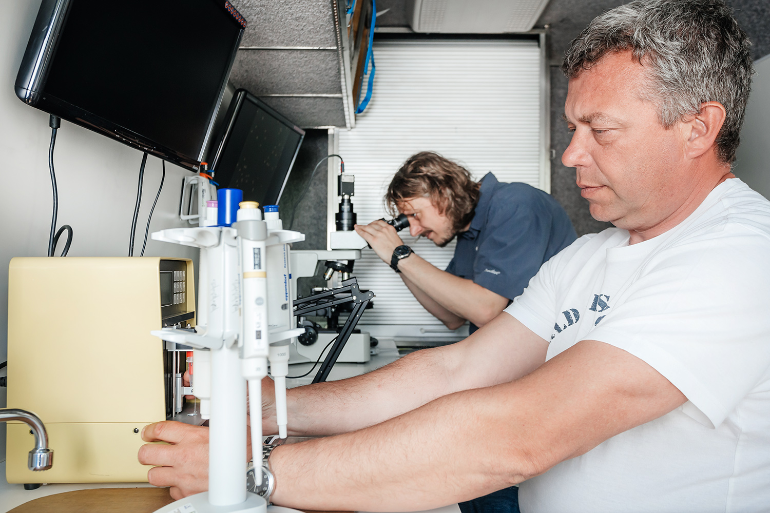 Dwóch naukowców podczas pracy badawczej w laboratorium – jeden przygotowuje aparaturę pomiarową, drugi prowadzi obserwację pod mikroskopem.